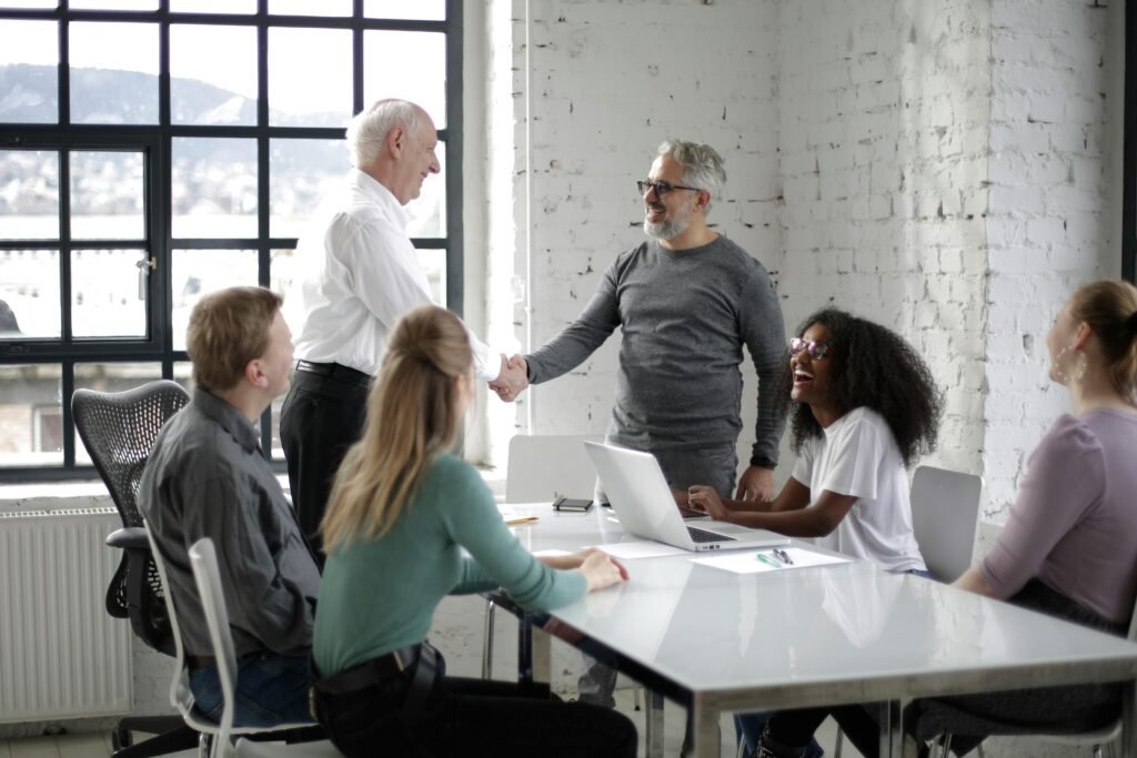 pexels photo 3931440 3931440 Cheerful male colleagues shaking hands while discussing business ideas with group of multiethnic coworkers gathering around table with gadgets and documents in modern light workspace